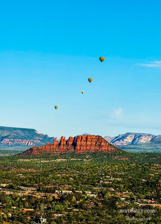 Hot air balloons rising over the hills and mountains of Sedona.